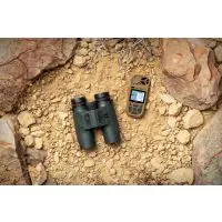 Black binoculars and a small handheld GPS device on a rocky, dirt-covered ground outdoors.