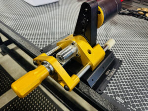 Yellow locking clamp gripping a metal shaft on a perforated worktable in a workshop sense